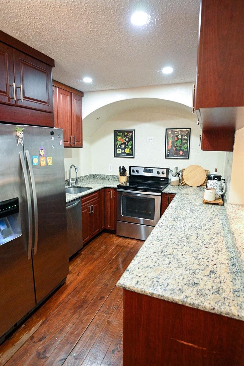 A kitchen features dark wood cabinets, granite countertops, stainless steel appliances, and hardwood flooring — 248 NE 41st Street, Deerfield Beach FL 33064, DEERFIELD BEACH, FL