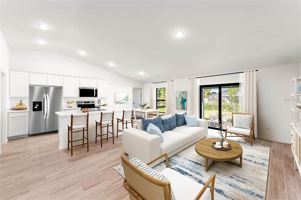 An open-concept living room and kitchen with white cabinetry, light wood flooring, and sliding doors — 11797 OCEANSPRAY BOULEVARD, ENGLEWOOD, FL