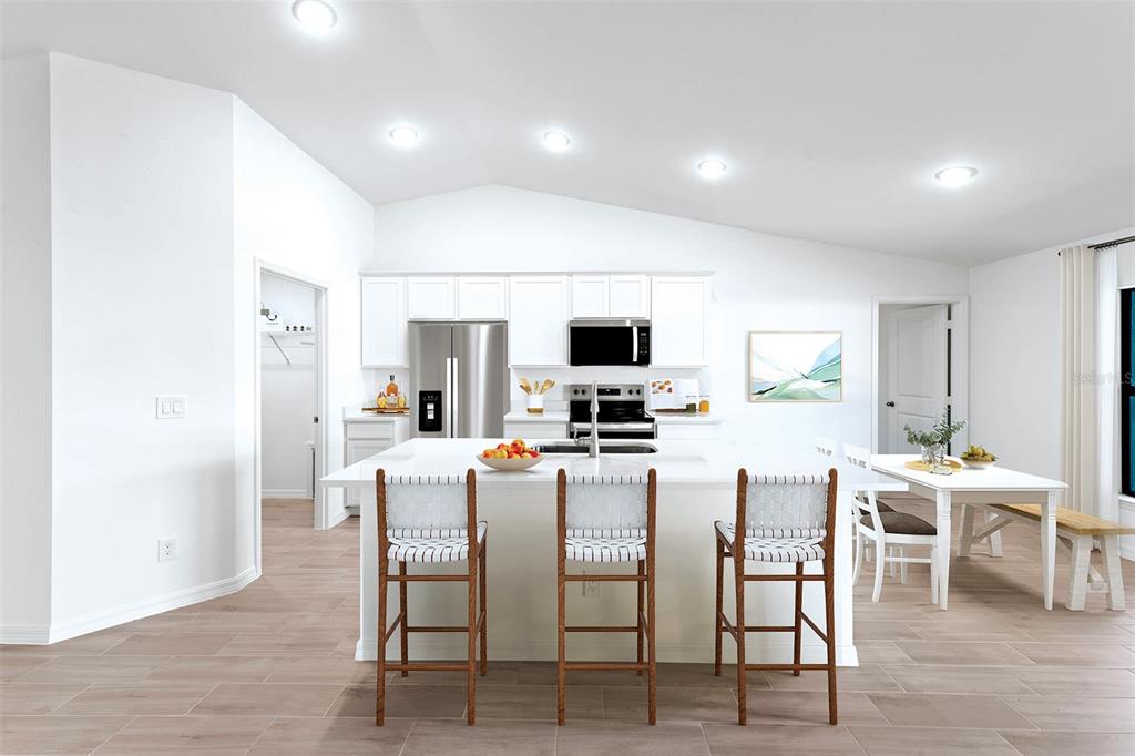 A bright, modern kitchen features white cabinetry, a large central island, and light wood flooring — 11797 OCEANSPRAY BOULEVARD, ENGLEWOOD, FL