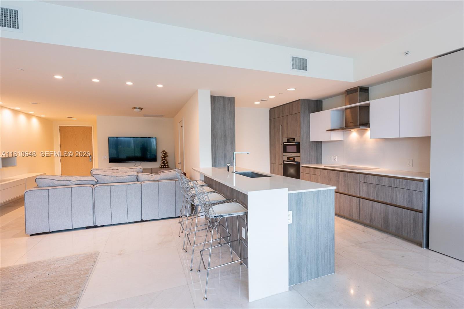 A modern open-concept kitchen features wood-grain cabinetry, a white island, and a living area — 360 Ocean Dr # 205S, Key Biscayne FL 33149, KEY BISCAYNE, FL