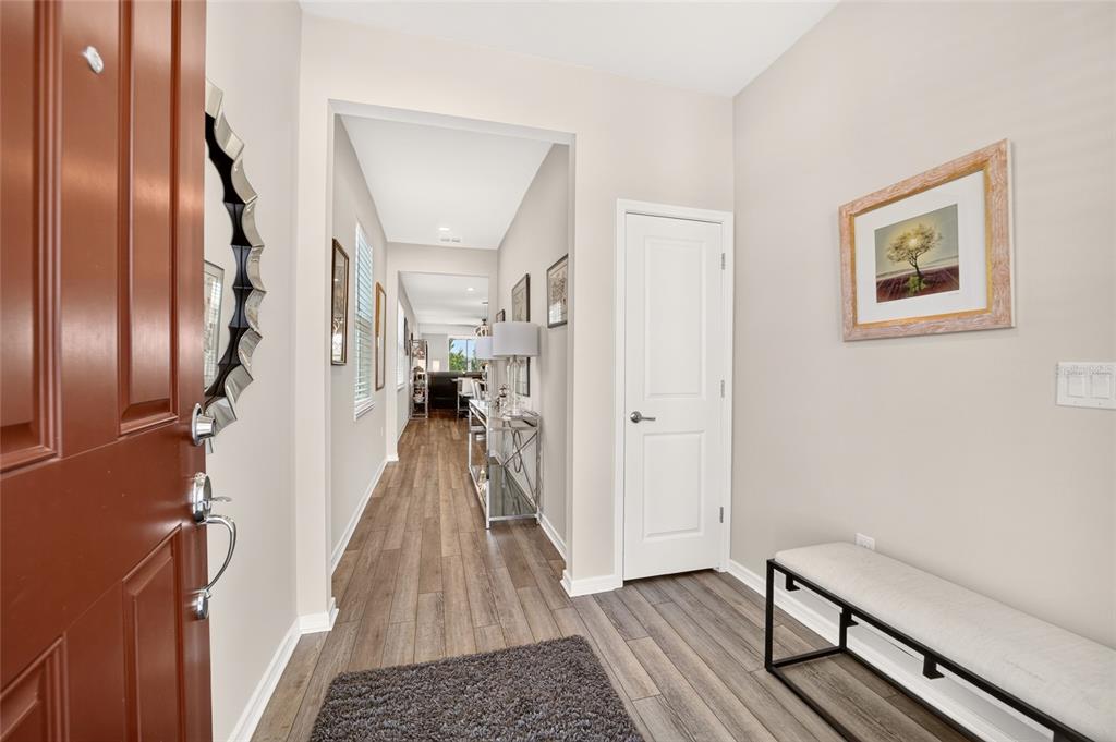 An entryway with wood-look flooring, a white door, a bench, and a view down the hallway — 6043 SW 93RD CIRCLE, OCALA, FL