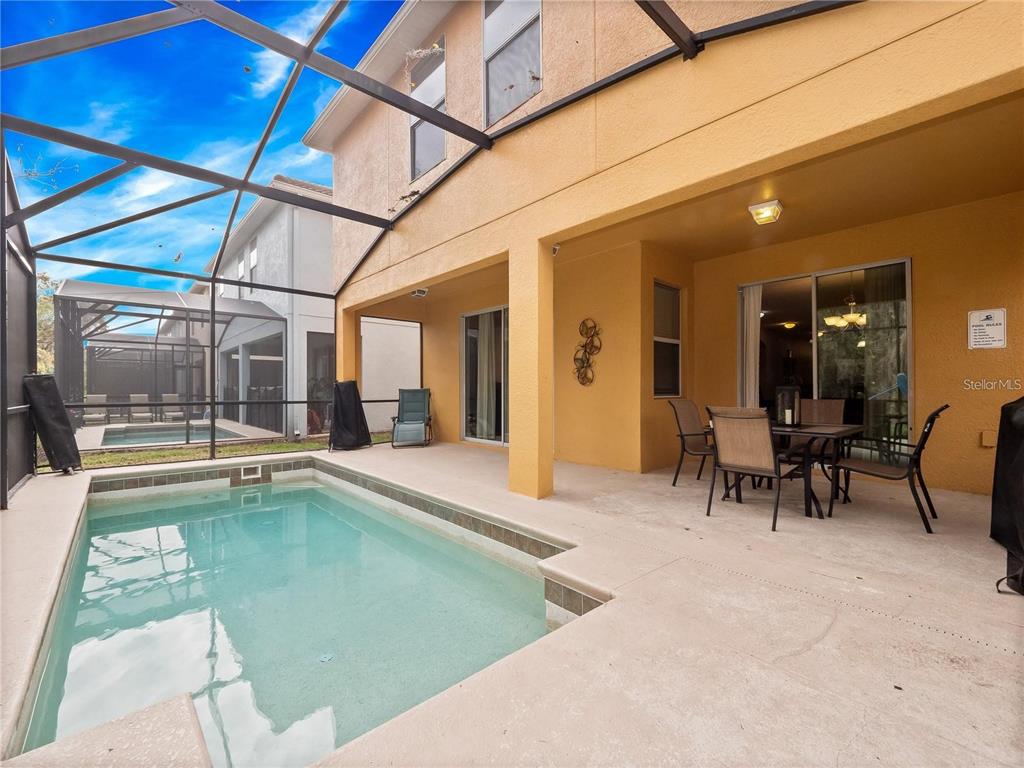 A screened-in patio features a small swimming pool and a dining set under a lanai — 8876 CANDY PALM ROAD, KISSIMMEE, FL
