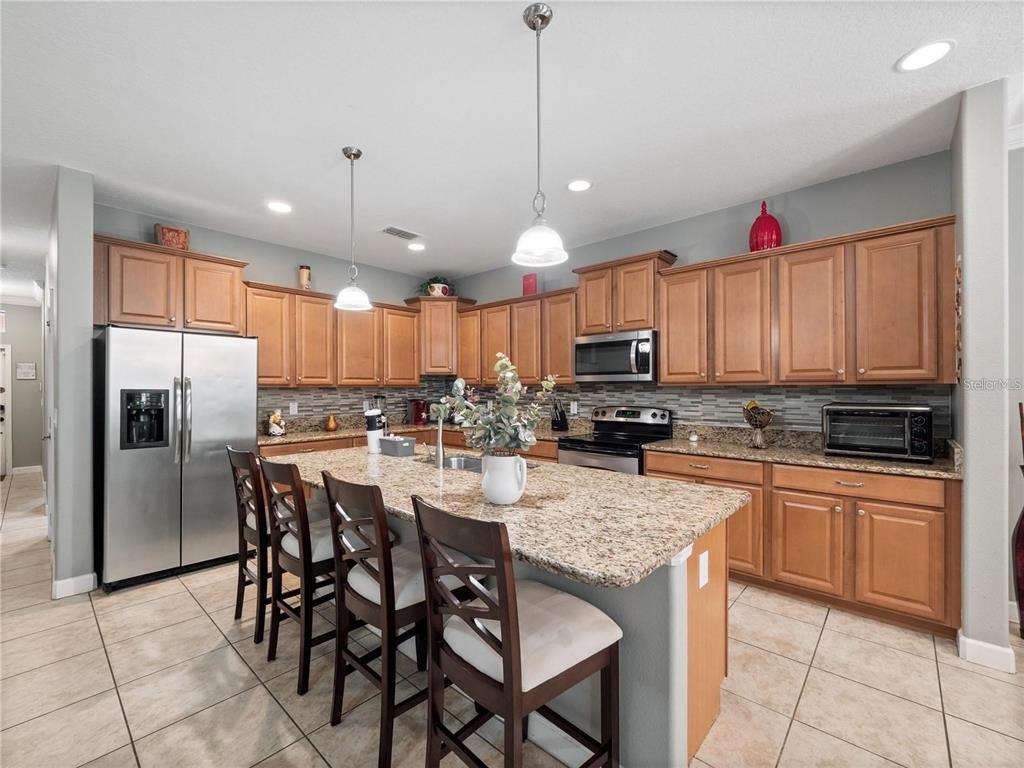A kitchen with wood cabinets, granite countertops, a center island, and stainless steel appliances — 8876 CANDY PALM ROAD, KISSIMMEE, FL