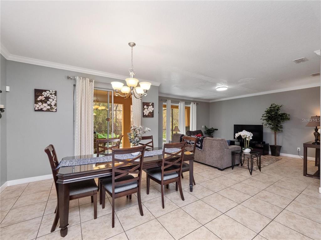 A dining area with a dark wood table and chairs opens into a living room — 8876 CANDY PALM ROAD, KISSIMMEE, FL