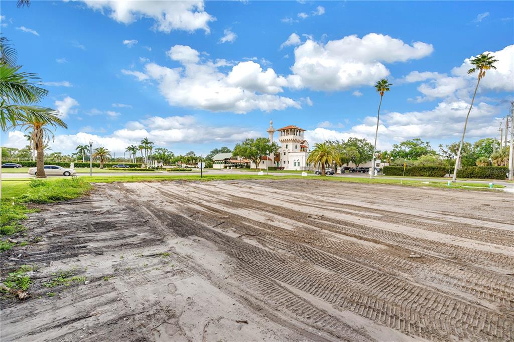 A vacant, dirt-covered lot sits in the foreground with a distant building and palm trees — 515 SNELL ISLE BOULEVARD NE, ST PETERSBURG, FL