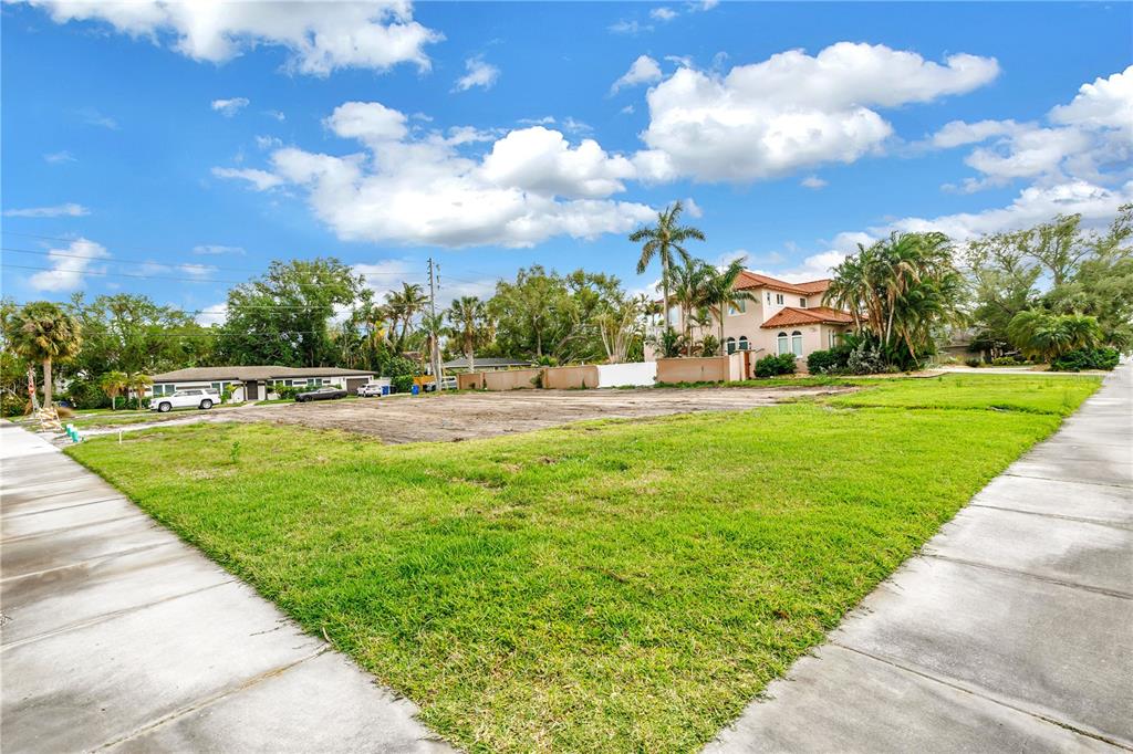 A vacant, grassy residential lot sits in a suburban neighborhood with trees and nearby houses — 515 SNELL ISLE BOULEVARD NE, ST PETERSBURG, FL