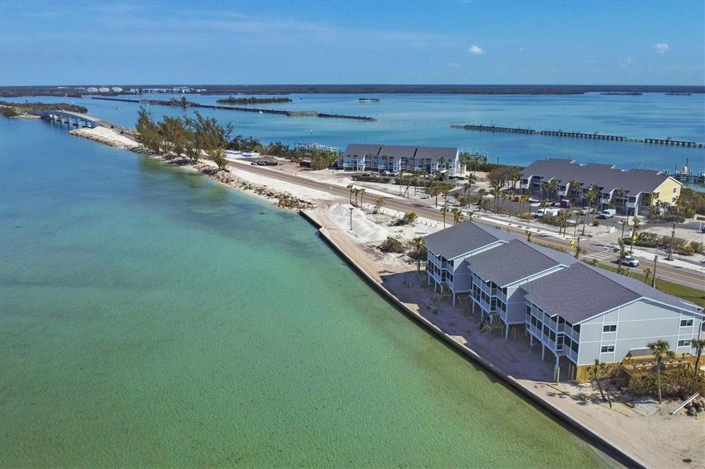 An aerial view shows multi-story buildings along a coastal road next to turquoise water — 6021 BOCA GRANDE CAUSEWAY UNIT G80, BOCA GRANDE, FL