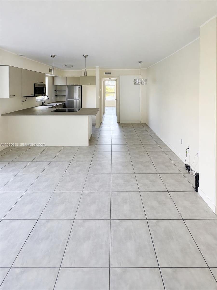 A kitchen with light-colored cabinets and a breakfast bar opens into a tiled living area — 777 NE 62nd St # C402, Miami FL 33138, MIAMI, FL