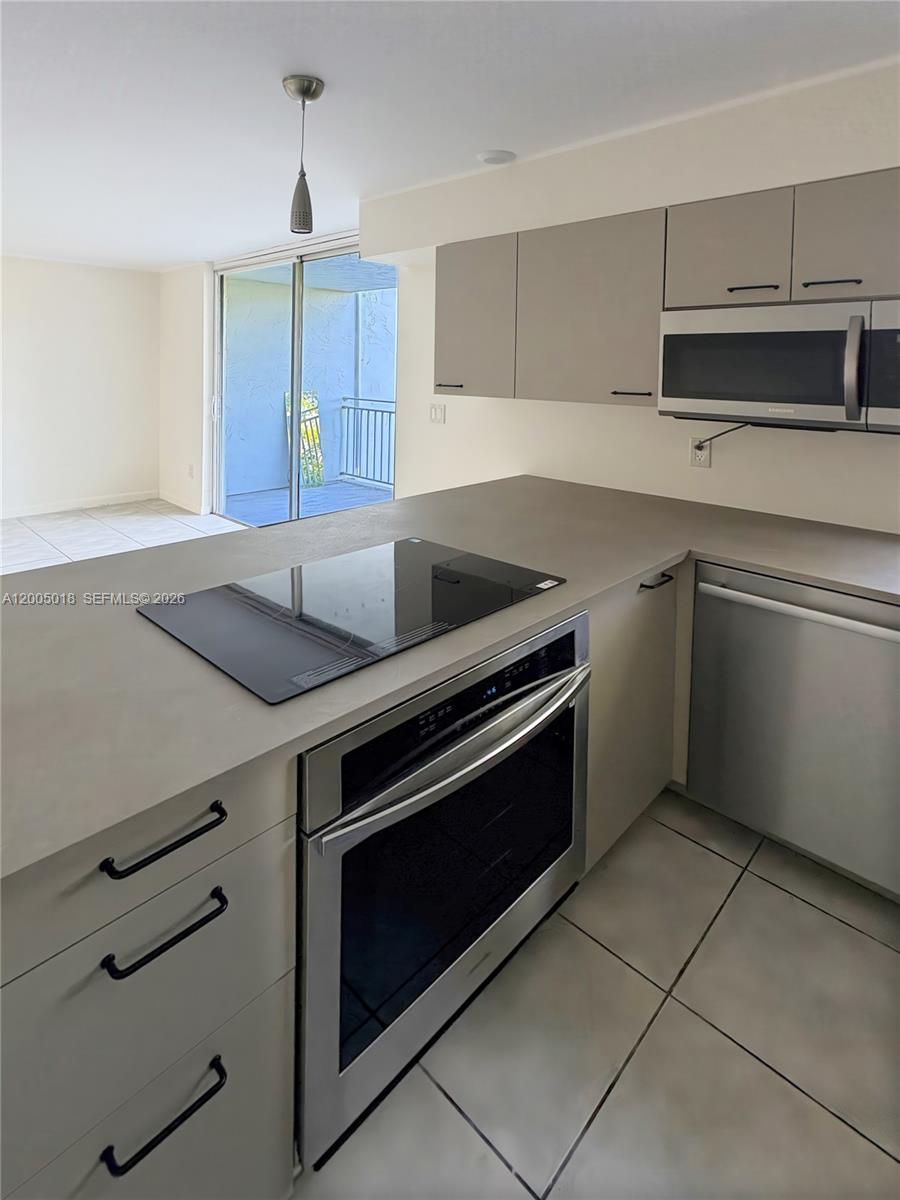 A kitchen features light gray cabinets, stainless steel appliances, and a glass cooktop island — 777 NE 62nd St # C402, Miami FL 33138, MIAMI, FL