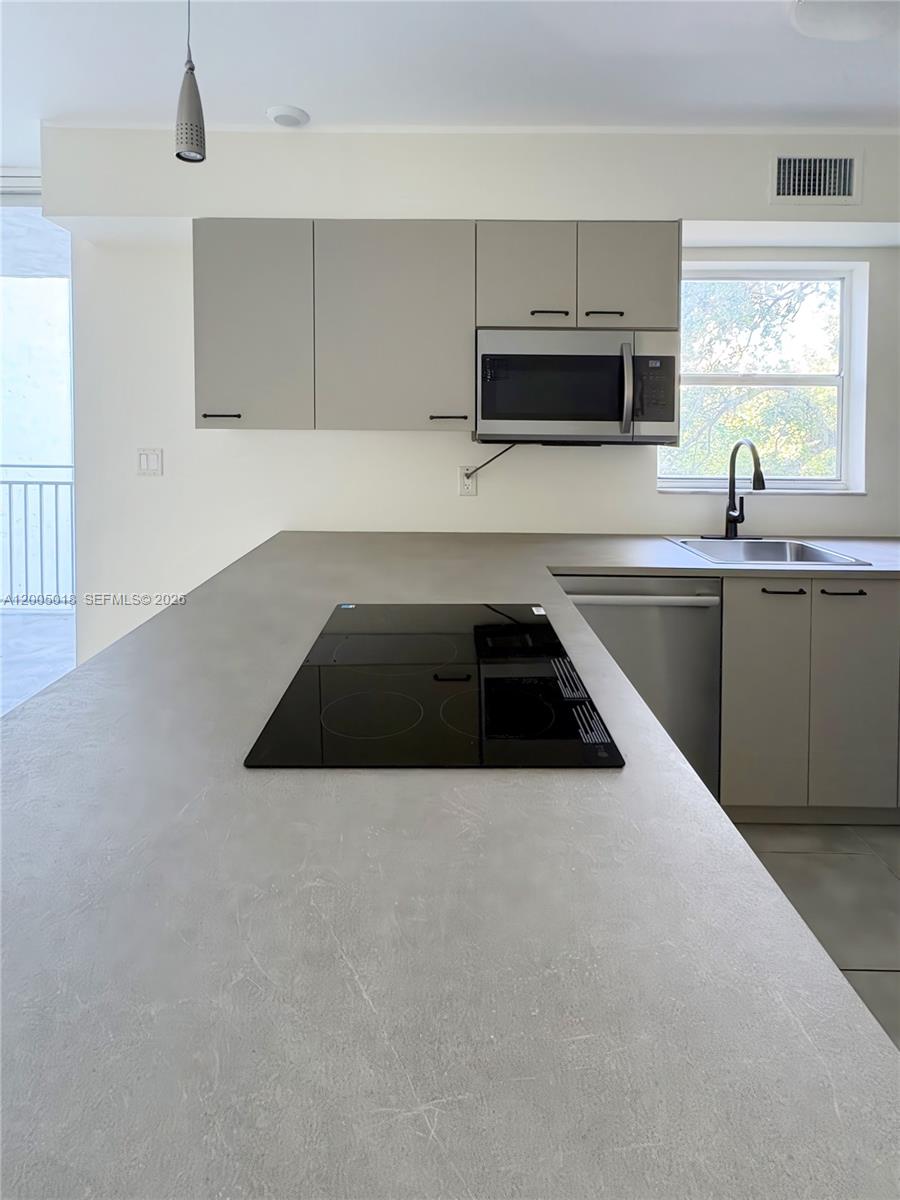 A kitchen features a gray island with a black cooktop, light cabinetry, and a window — 777 NE 62nd St # C402, Miami FL 33138, MIAMI, FL