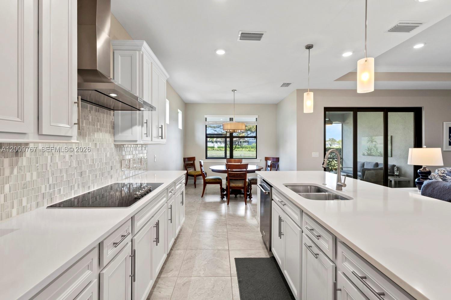 A modern kitchen features white cabinetry, quartz countertops, a tile backsplash, and a dining area — 6359 Achievement, Ave Maria FL 34142, AVE MARIA, FL