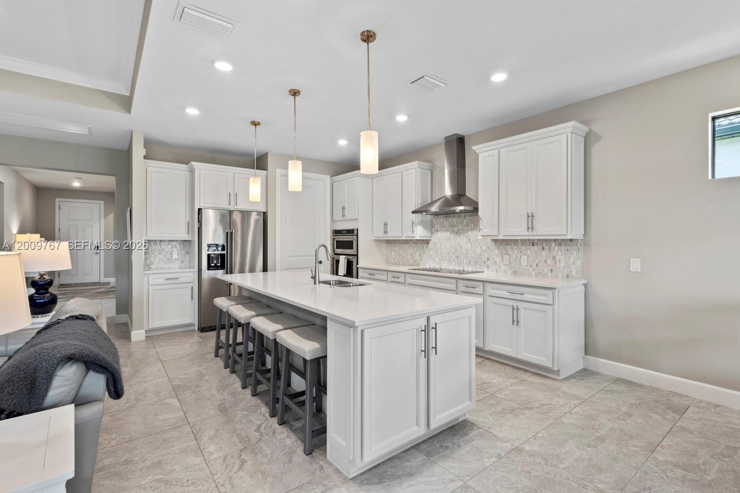 A modern kitchen features white cabinetry, a large central island with seating, and tile flooring — 6359 Achievement, Ave Maria FL 34142, AVE MARIA, FL