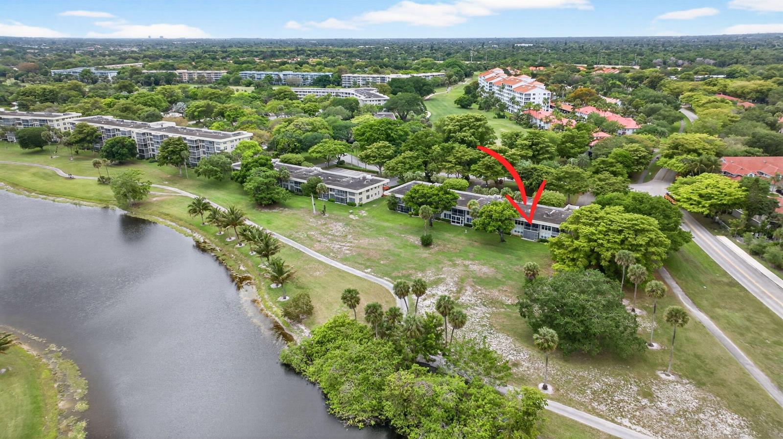 An aerial view shows a multi-story apartment building situated near a lake and trees — 800 Cypress Boulevard # 204a, Pompano Beach FL 33069, POMPANO BEACH, FL