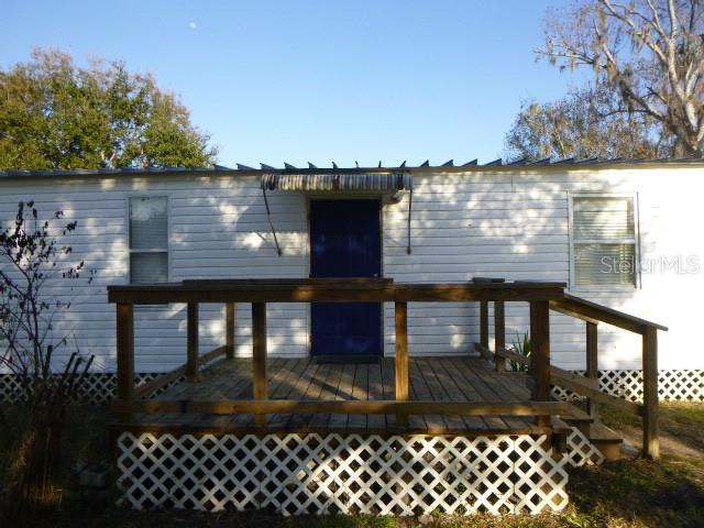 A mobile home exterior features a wooden deck with lattice skirting and a blue door — 6616 MANGROVE DRIVE, WESLEY CHAPEL, FL