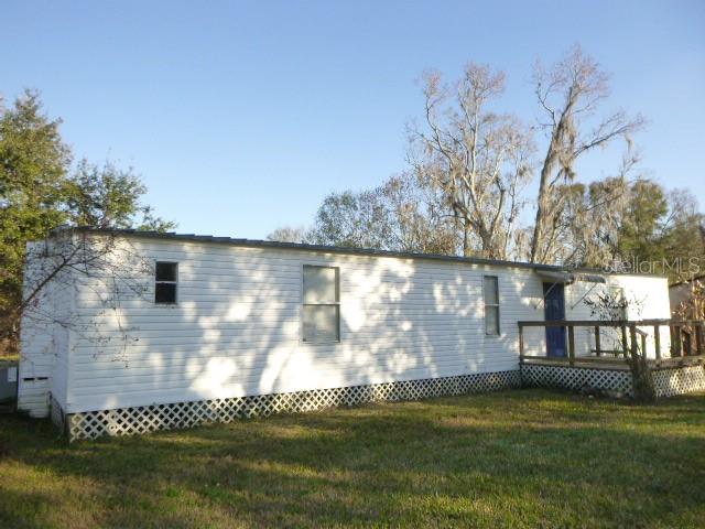 A white mobile home with a wooden deck stands in a grassy yard under trees — 6616 MANGROVE DRIVE, WESLEY CHAPEL, FL