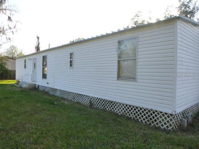 The exterior of a white mobile home features vinyl siding, a lattice skirt, and several windows — 6616 MANGROVE DRIVE, WESLEY CHAPEL, FL