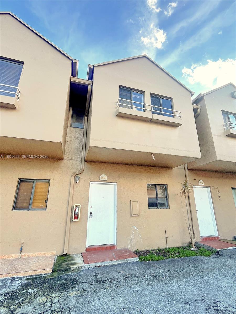 A two-story tan stucco townhouse exterior features a white front door and metal railings — 5712 W 25th Ct # 5712, Hialeah FL 33016, HIALEAH, FL