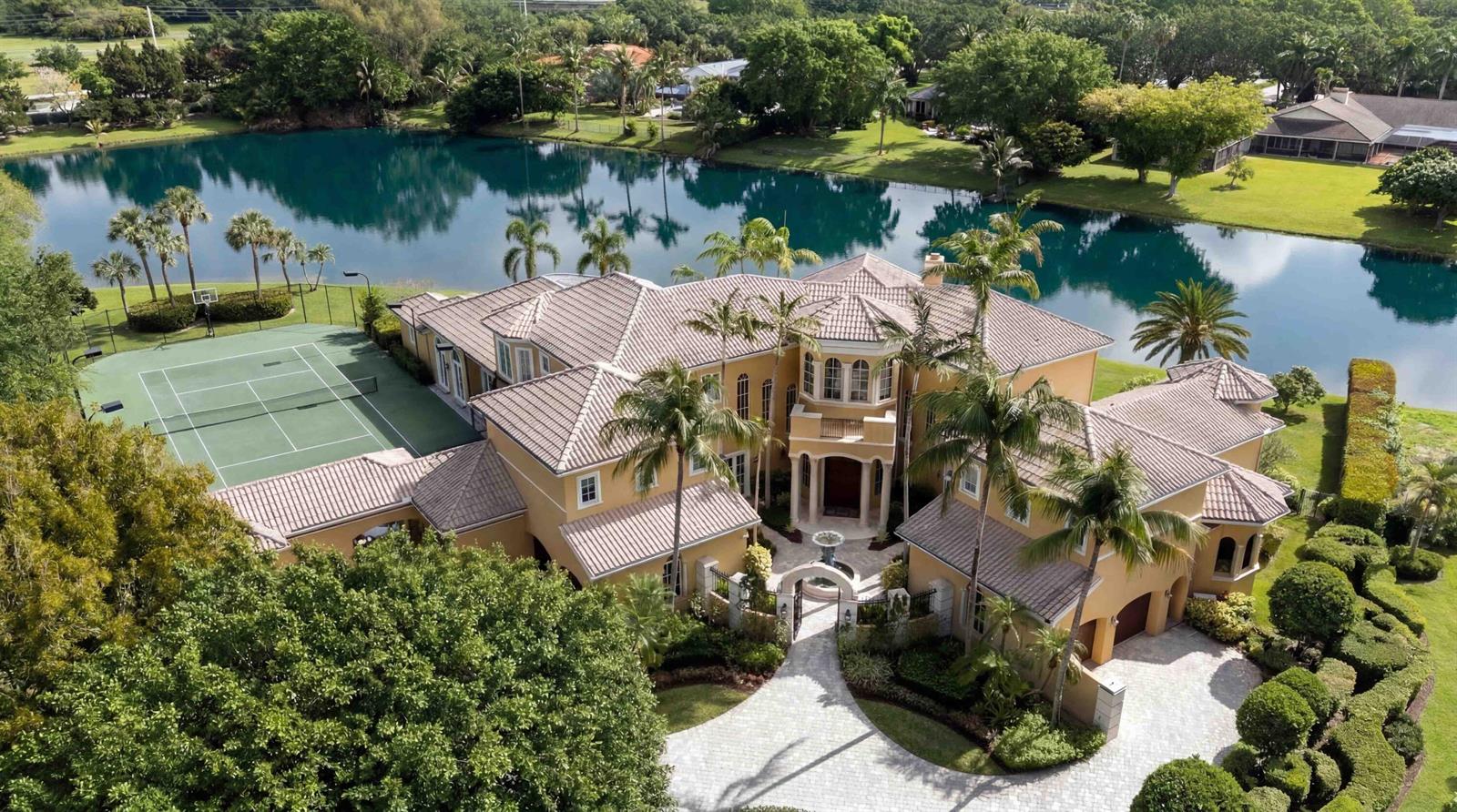 An aerial view of a large yellow mansion with a tennis court and a lake — 18118 Daybreak Drive, Boca Raton FL 33496, BOCA RATON, FL