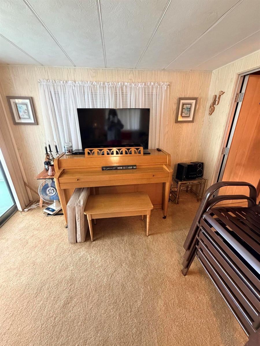 A living room features wood-paneled walls, tan carpeting, a piano with a television, and curtains — 5603 Lagoon Drive, Dania Beach FL 33312, DANIA BEACH, FL