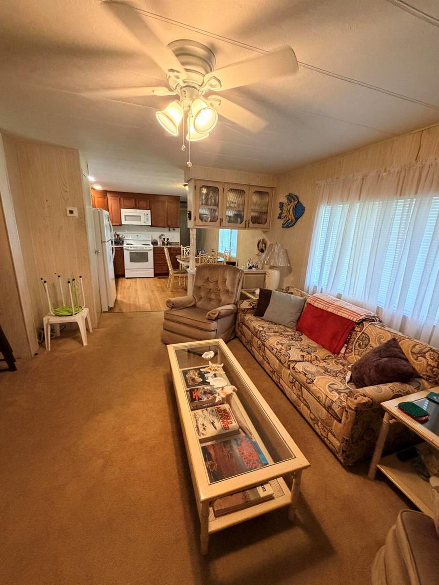A living room with beige carpet, a patterned sofa, a glass coffee table, and an open kitchen — 5603 Lagoon Drive, Dania Beach FL 33312, DANIA BEACH, FL