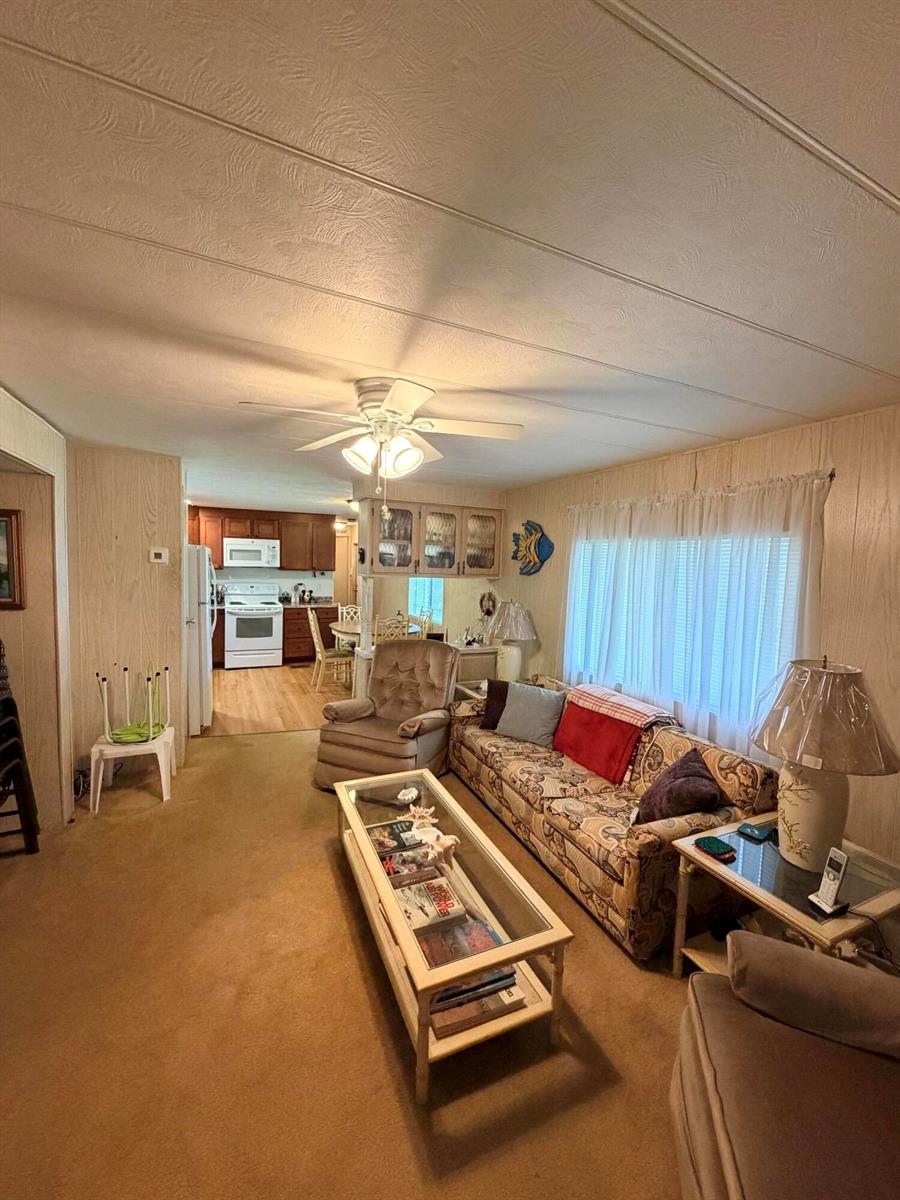 A living room with tan carpet, wood-paneled walls, a patterned sofa, and an adjacent kitchen — 5603 Lagoon Drive, Dania Beach FL 33312, DANIA BEACH, FL