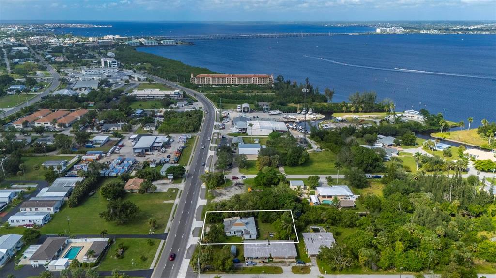 An aerial view shows a house with a white roof situated near a coastal road — 25158 MARION AVENUE, PUNTA GORDA, FL