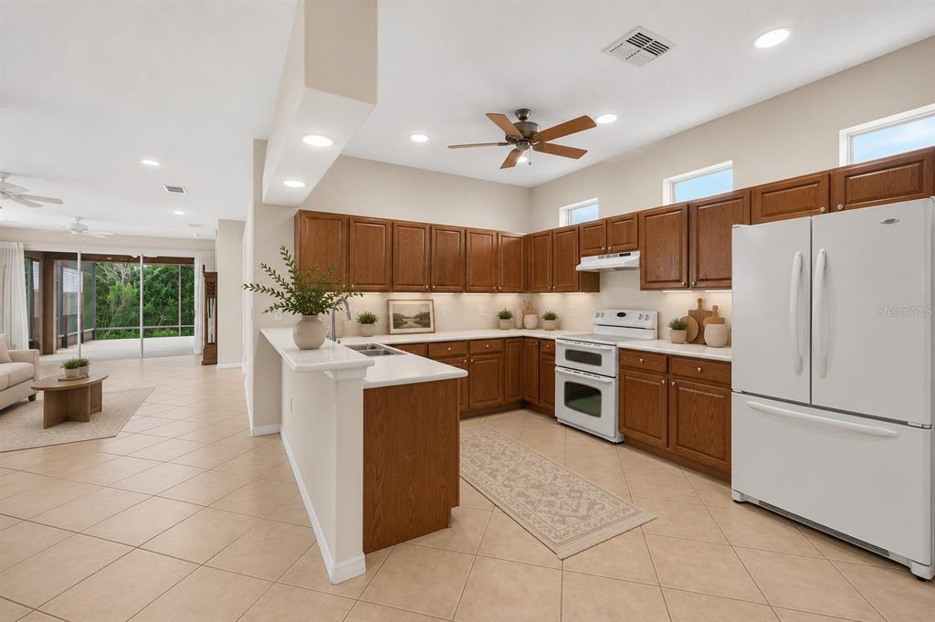 A kitchen with wood cabinets, white countertops, and white appliances opens to a living area — 20931 DIAMONTE DRIVE, LAND O LAKES, FL