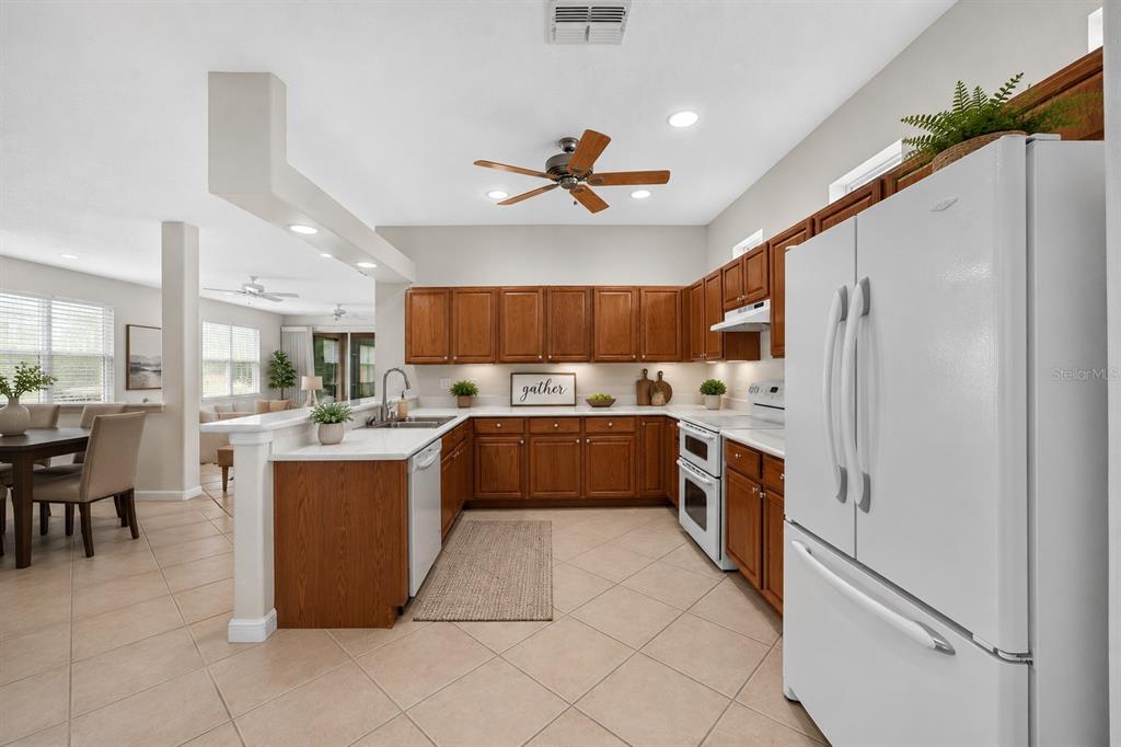 A kitchen with wood cabinets, white countertops, and tile flooring opens to a dining area — 20931 DIAMONTE DRIVE, LAND O LAKES, FL