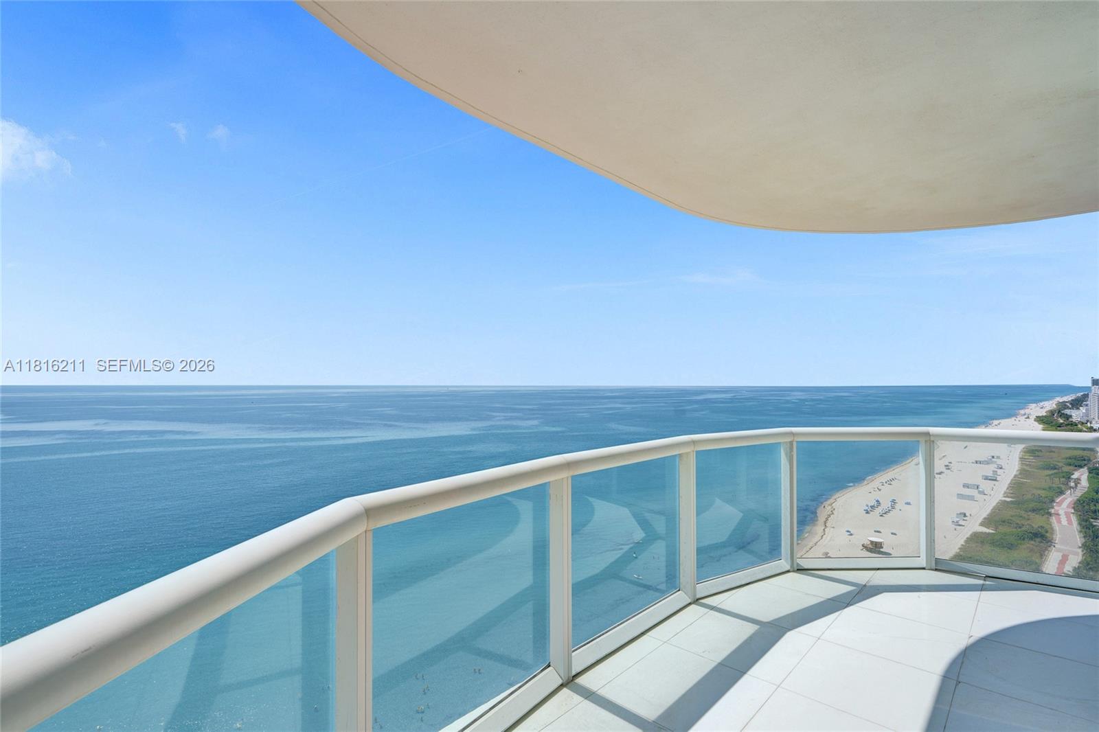 A high-rise balcony with a glass railing overlooks the ocean and a sandy beach — 6365 Collins Ave # 2403, Miami Beach FL 33141, MIAMI BEACH, FL