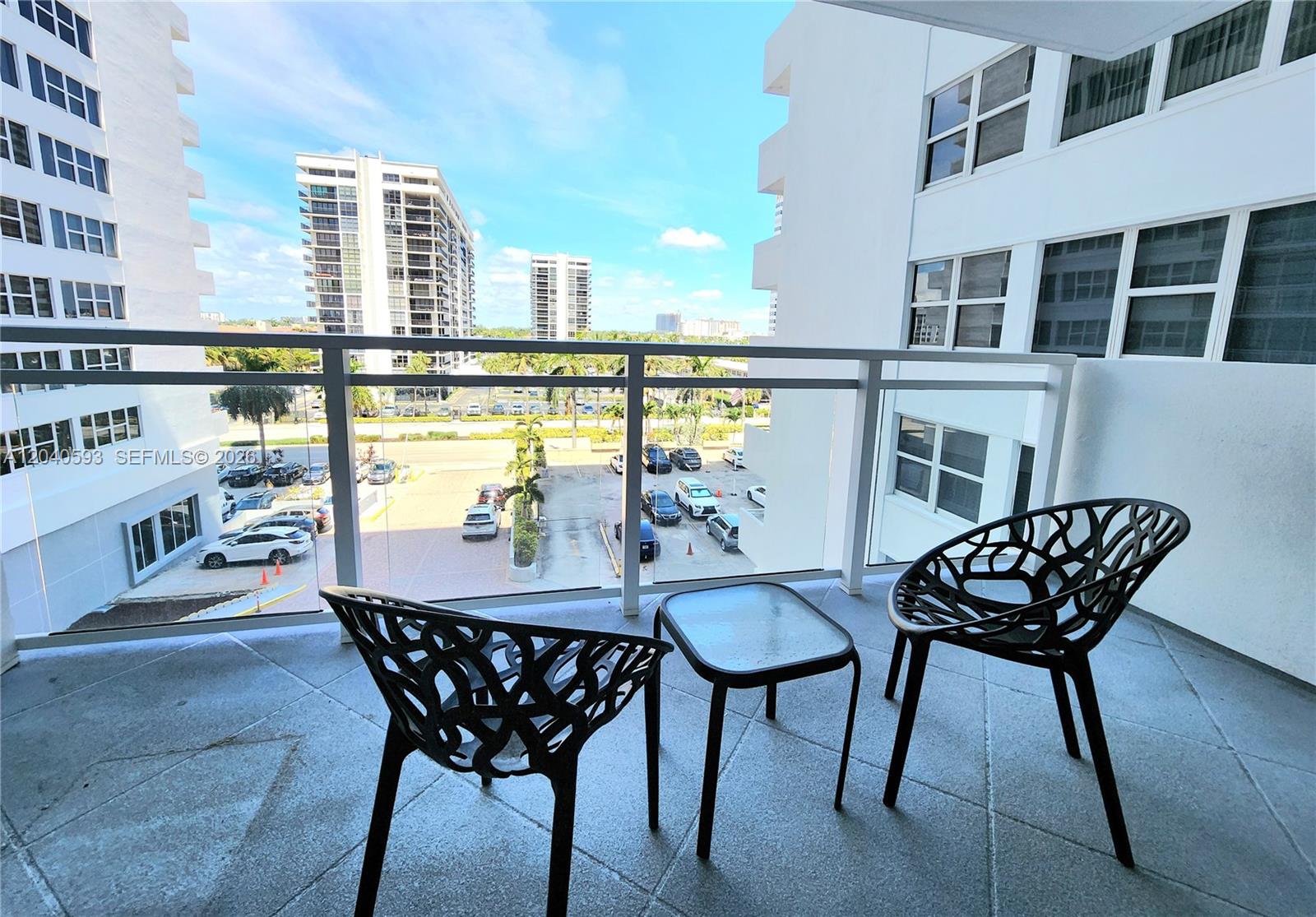 A balcony features two black patterned chairs, a small glass table, and a parking lot view — 2030 S Ocean Dr # 401, Hallandale Beach FL 33009, HALLANDALE BEACH, FL