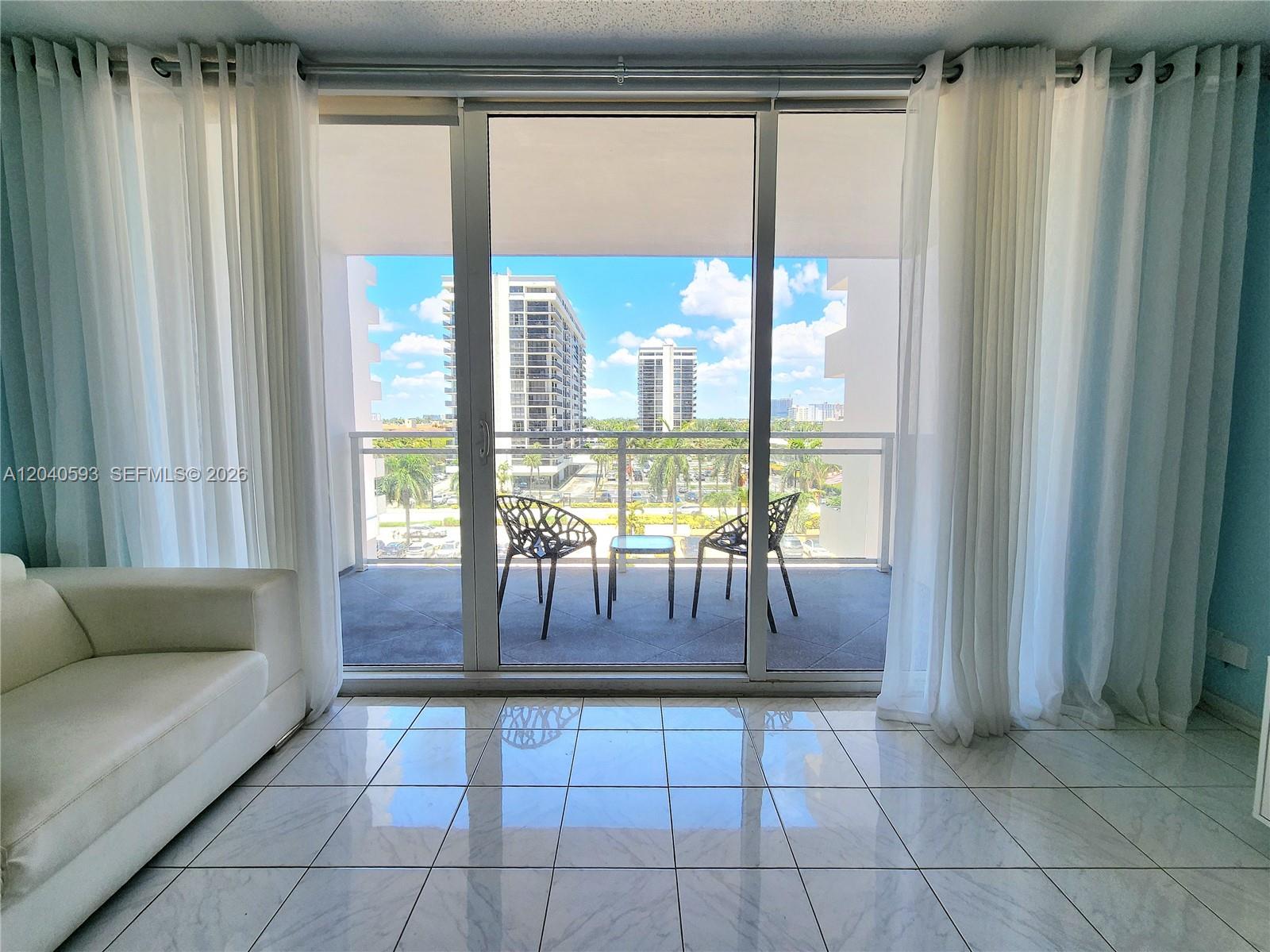 A living room with white tile floors opens through sliding glass doors to a balcony — 2030 S Ocean Dr # 401, Hallandale Beach FL 33009, HALLANDALE BEACH, FL