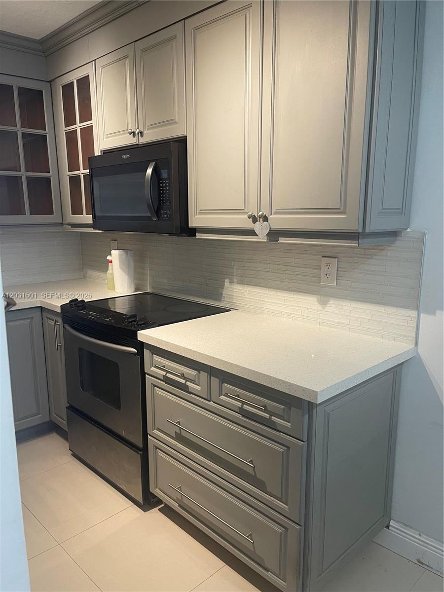 A kitchen features gray cabinets, stainless steel appliances, and light-colored countertops with a tiled backsplash — 7505 SW 82nd St # 212, Miami FL 33143, MIAMI, FL