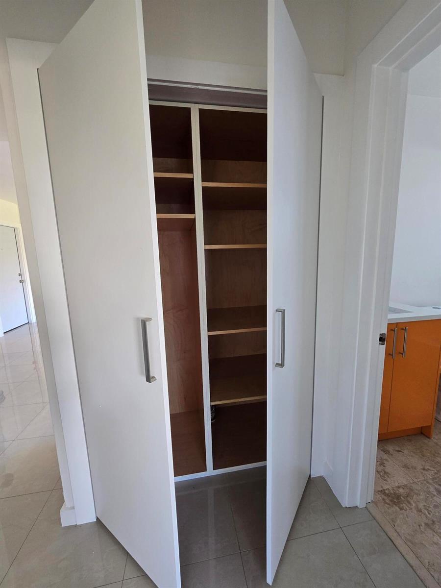 A white double-door closet with interior wooden shelving stands in a tiled hallway — 201 SE 6th Avenue # 16, Pompano Beach FL 33060, POMPANO BEACH, FL