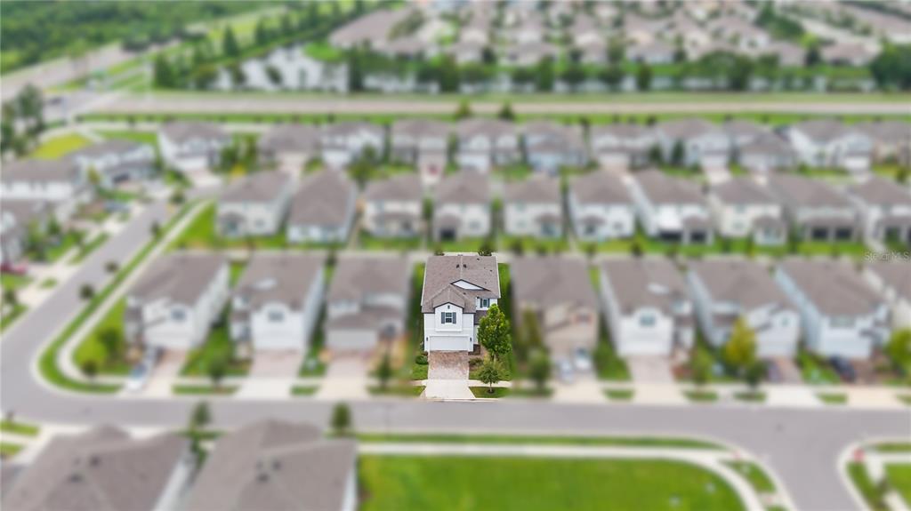 An aerial view shows a two-story suburban house with a paved driveway and surrounding neighborhood — 7421 NOTCHED PINE BEND, WESLEY CHAPEL, FL