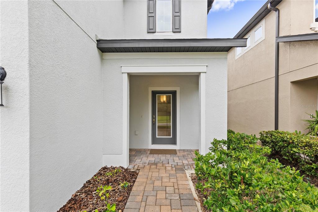 A paved walkway leads to the covered front entrance of a white stucco house — 7421 NOTCHED PINE BEND, WESLEY CHAPEL, FL