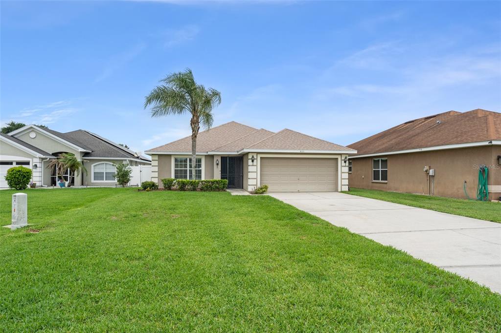 A single-story suburban house with a tan exterior, a two-car garage, and a palm tree — 4111 ISLAND LAKES DRIVE, WINTER HAVEN, FL