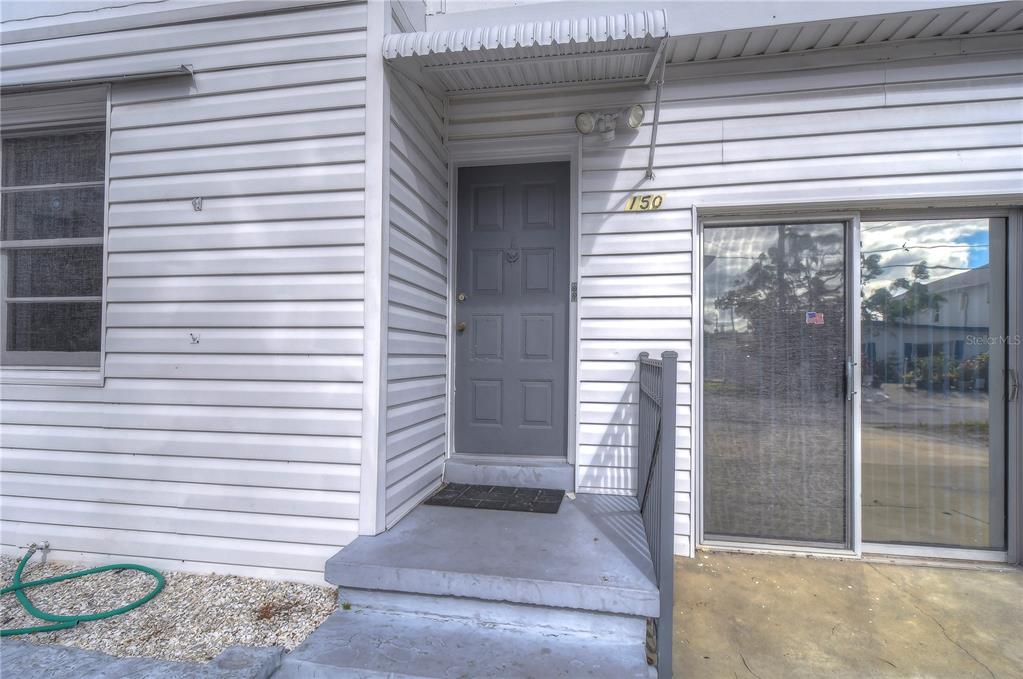 The exterior of a residential unit features a gray front door, steps, and sliding glass doors — 150 E MADEIRA AVENUE UNIT 3, MADEIRA BEACH, FL