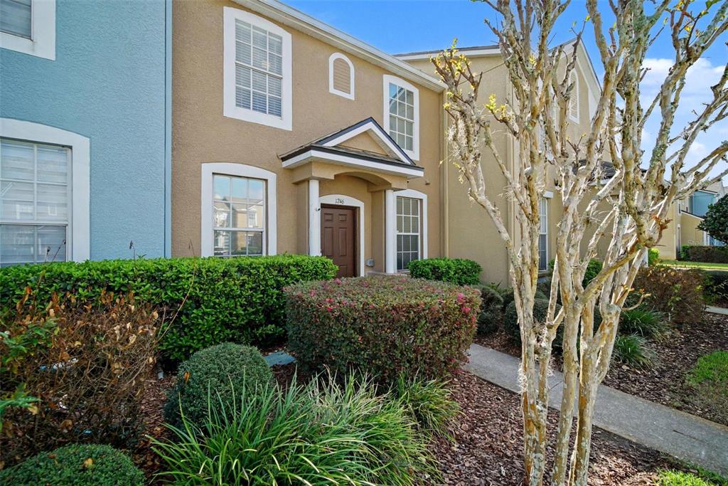 A tan two-story townhouse with a brown front door and a small covered entryway — 1246 CHARLESWORTH DRIVE, WESLEY CHAPEL, FL