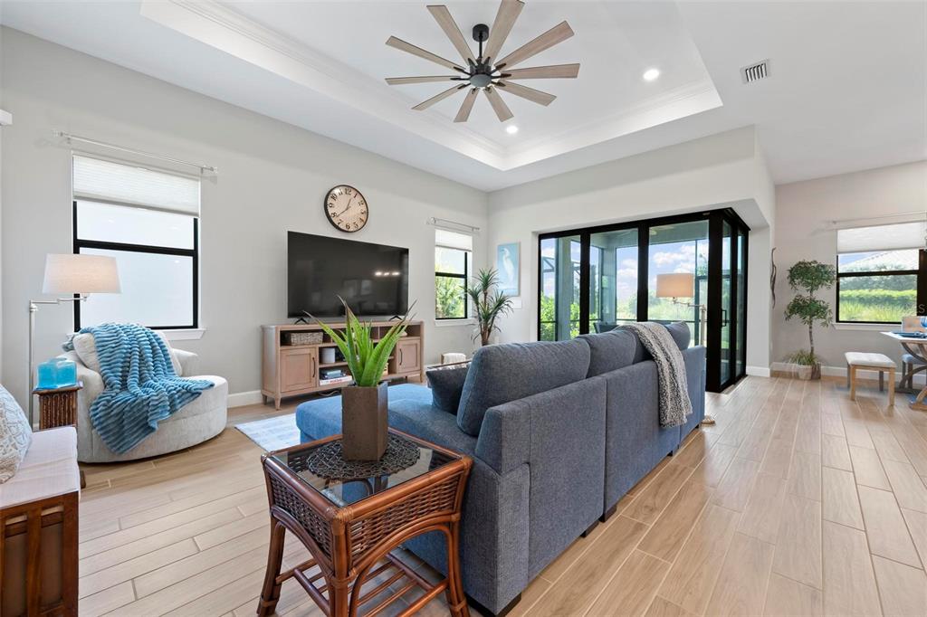 A living room features a tray ceiling, ceiling fan, blue sofa, and large sliding glass doors — 6205 GRANDE TALON LANE, NOKOMIS, FL