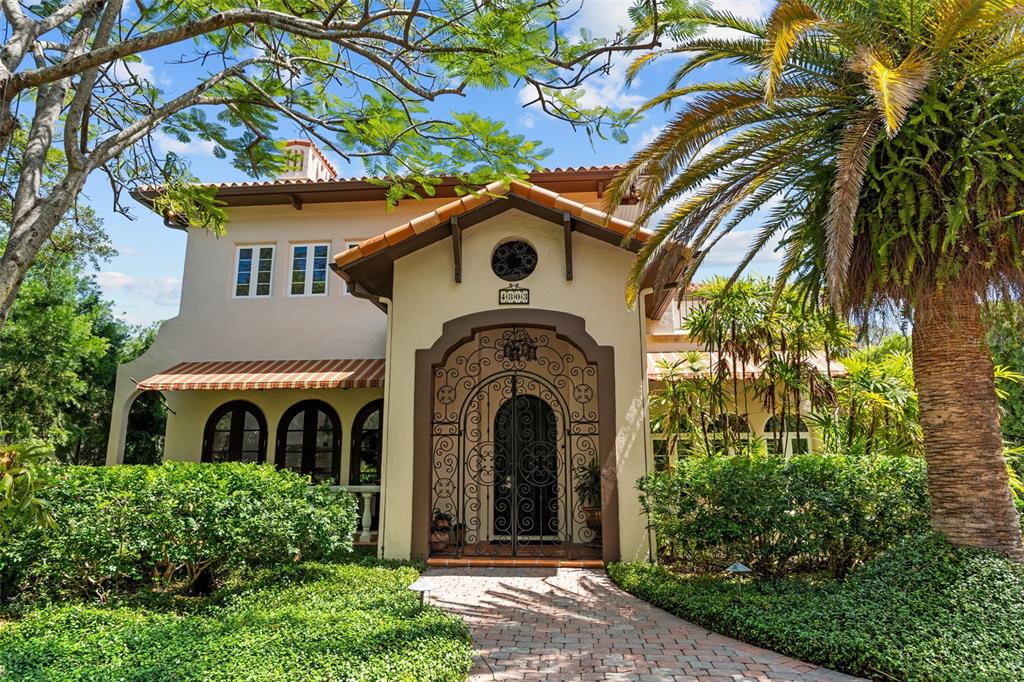 A two-story Mediterranean-style house features a decorative iron gate entrance and a paved walkway — 4803 W WOODMERE ROAD, TAMPA, FL