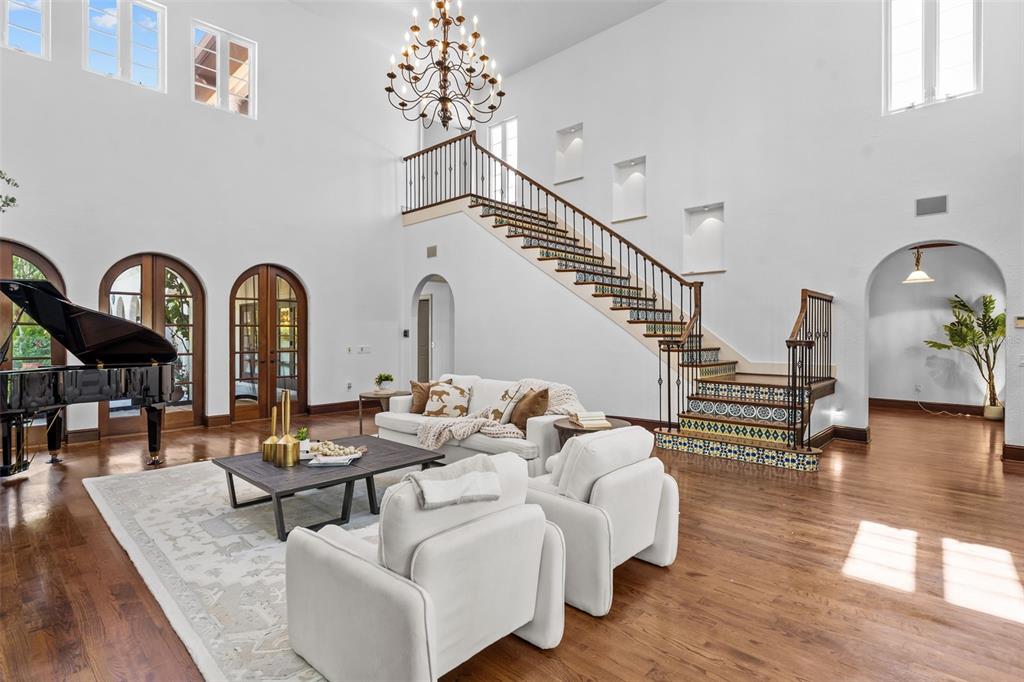 A grand living room features a piano, a tiled staircase, and a large chandelier — 4803 W WOODMERE ROAD, TAMPA, FL