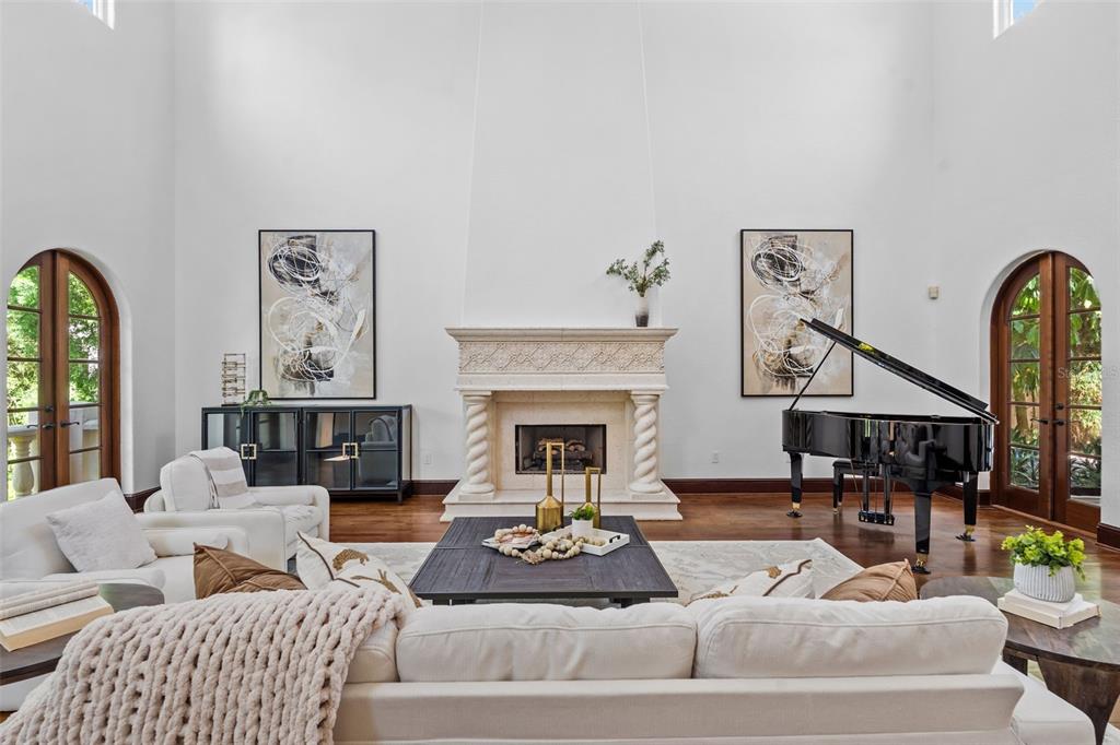 A spacious living room features a tall fireplace, a grand piano, and arched glass doors — 4803 W WOODMERE ROAD, TAMPA, FL