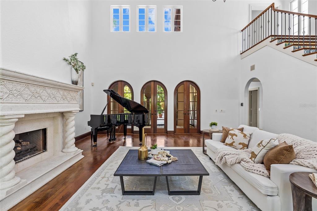 A high-ceilinged living room features a grand piano, fireplace, arched doors, and a staircase — 4803 W WOODMERE ROAD, TAMPA, FL