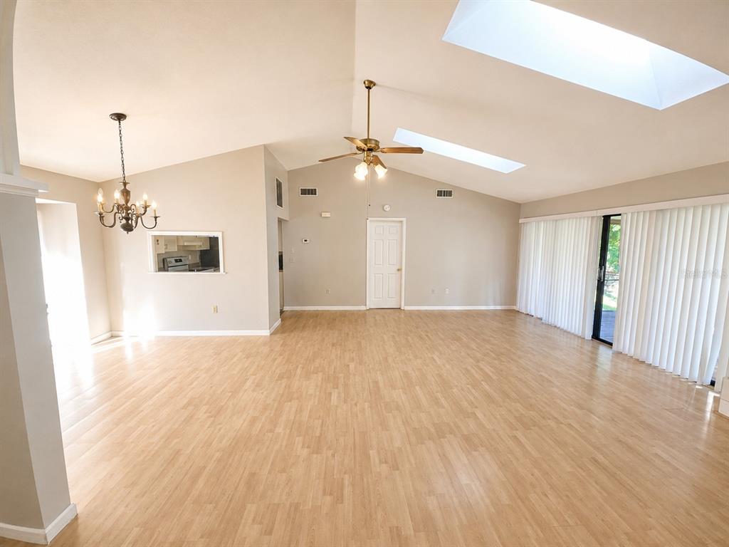 A spacious living room features light wood flooring, vaulted ceilings with skylights, and a chandelier — 700 SOUTH VENICE AVENUE, VENICE, FL
