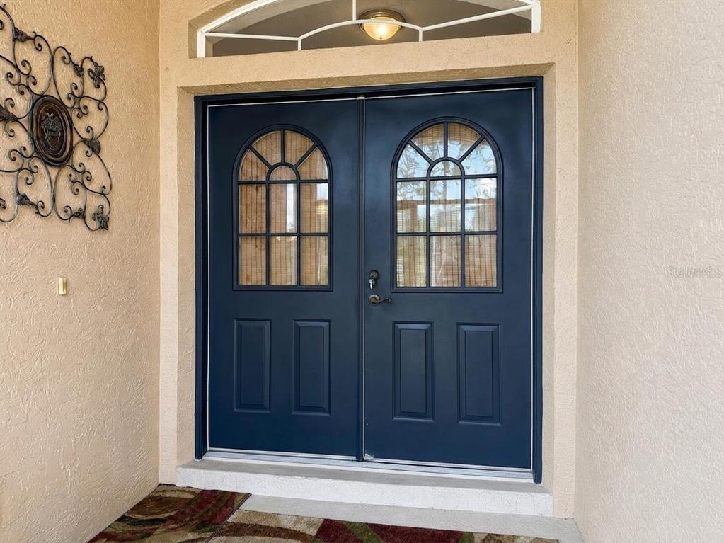 A dark blue double front door with arched glass windows sits under a transom window — 1487 EVANGELINA LANE, NORTH PORT, FL