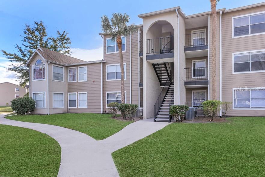 A three-story apartment building with beige siding, exterior staircases, and a concrete walkway — 4760 WALDEN CIRCLE UNIT 5-31, ORLANDO, FL