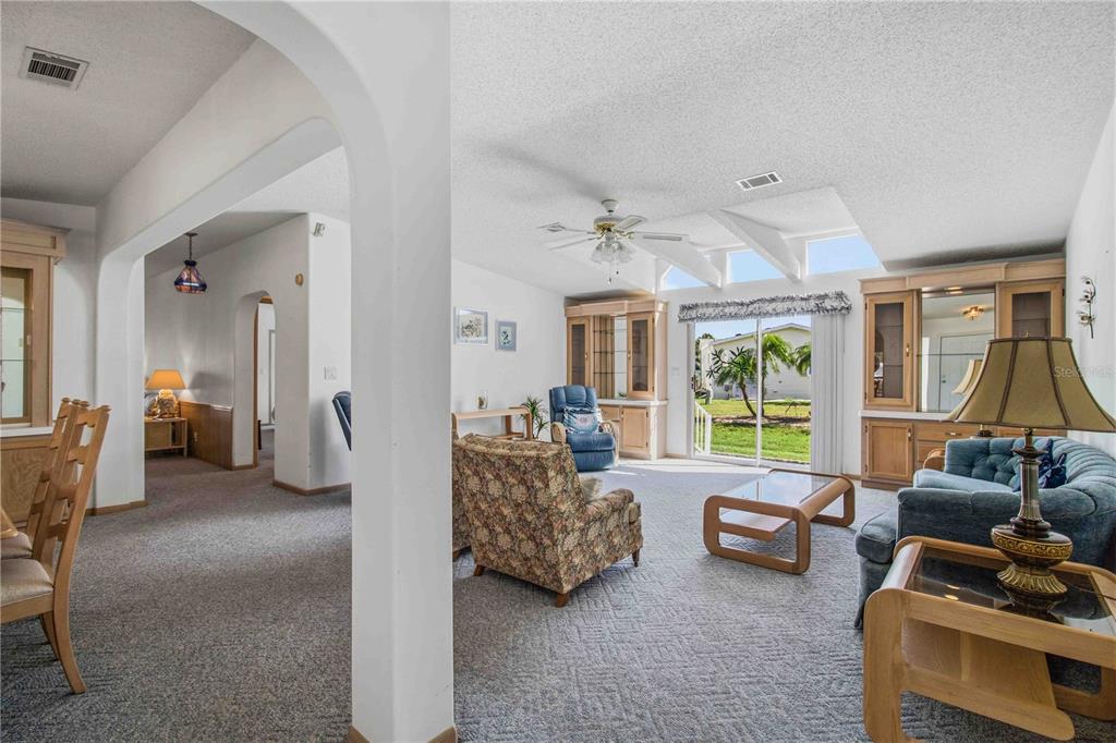 A living room with carpeted floors, vaulted ceilings, built-in cabinetry, and a sliding glass door — 8476 IMPERIAL CIRCLE, PALMETTO, FL