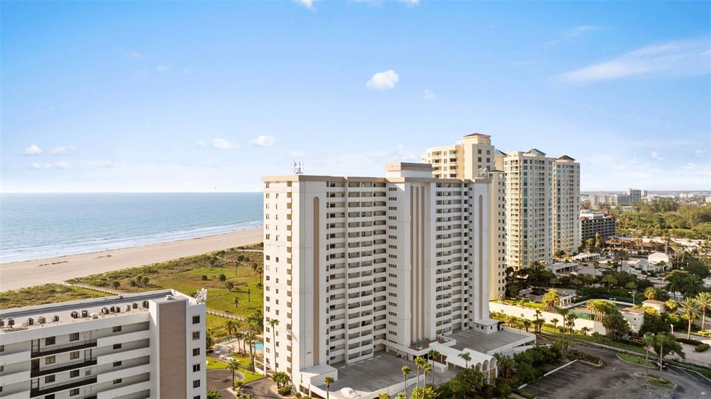 An aerial view shows high-rise residential buildings situated along a sandy beach and ocean — 1230 GULF BLVD UNIT 1204, CLEARWATER, FL