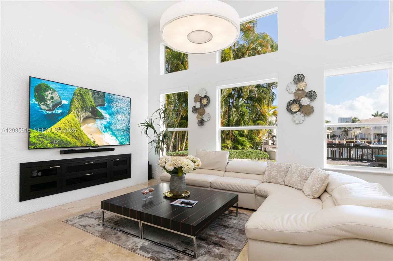 A bright living room features a large television, white sectional sofa, and floor-to-ceiling windows — 954 Sanibel Dr # 954, Hollywood FL 33019, HOLLYWOOD, FL