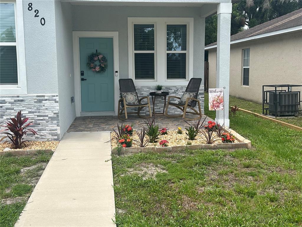 A light blue house exterior features a front porch with two chairs and landscaping — 820 PECAN AVENUE, SANFORD, FL